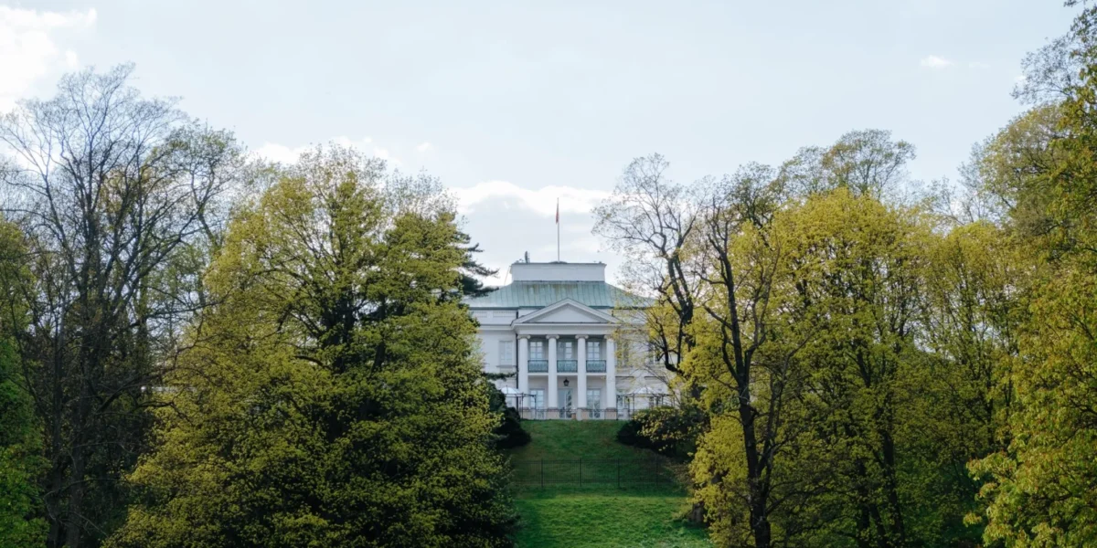 A picturesque view of Belweder Palace in Warsaw surrounded by lush spring foliage.