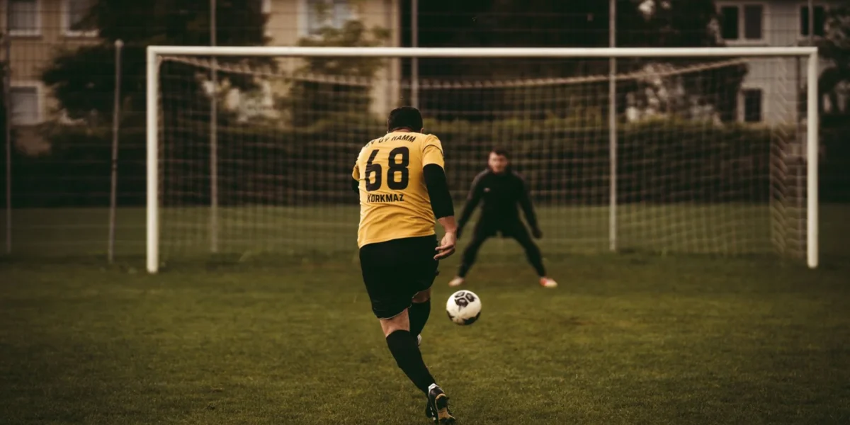 A soccer player takes a decisive penalty kick aiming to score against the goalkeeper.