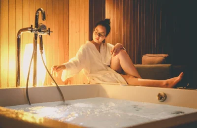 Woman sitting by a jacuzzi in a hotel room, enjoying relaxation indoors.
