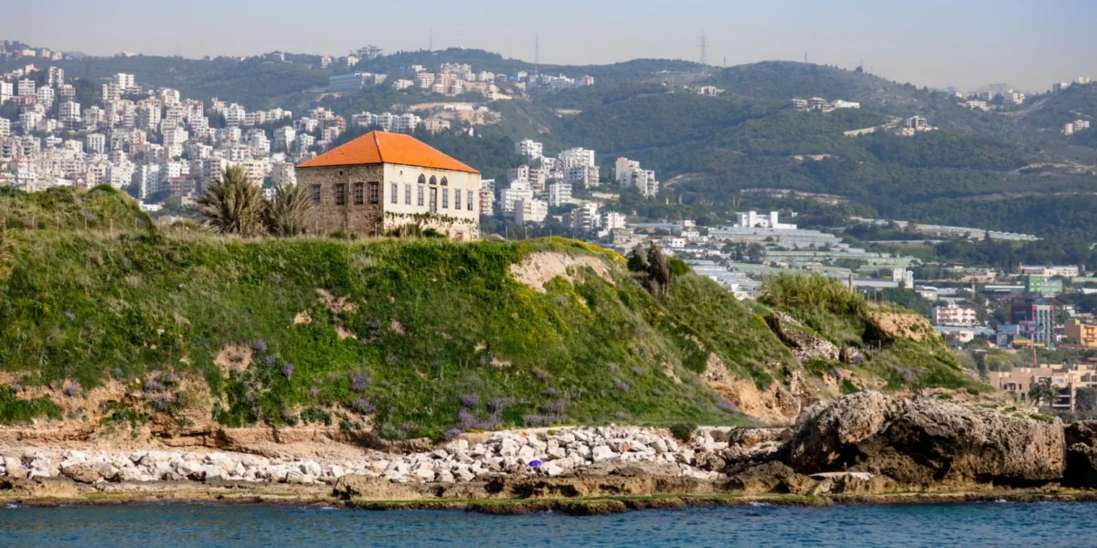 Scenic view of a historic building on a Lebanese coastline with city backdrop.