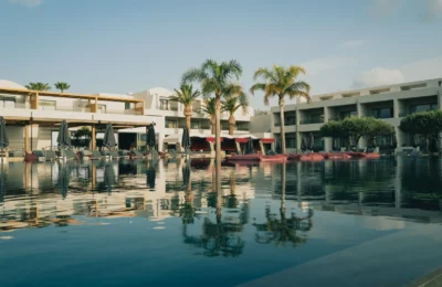 Elegant resort with a pool and palm trees under a clear blue sky in Greece.