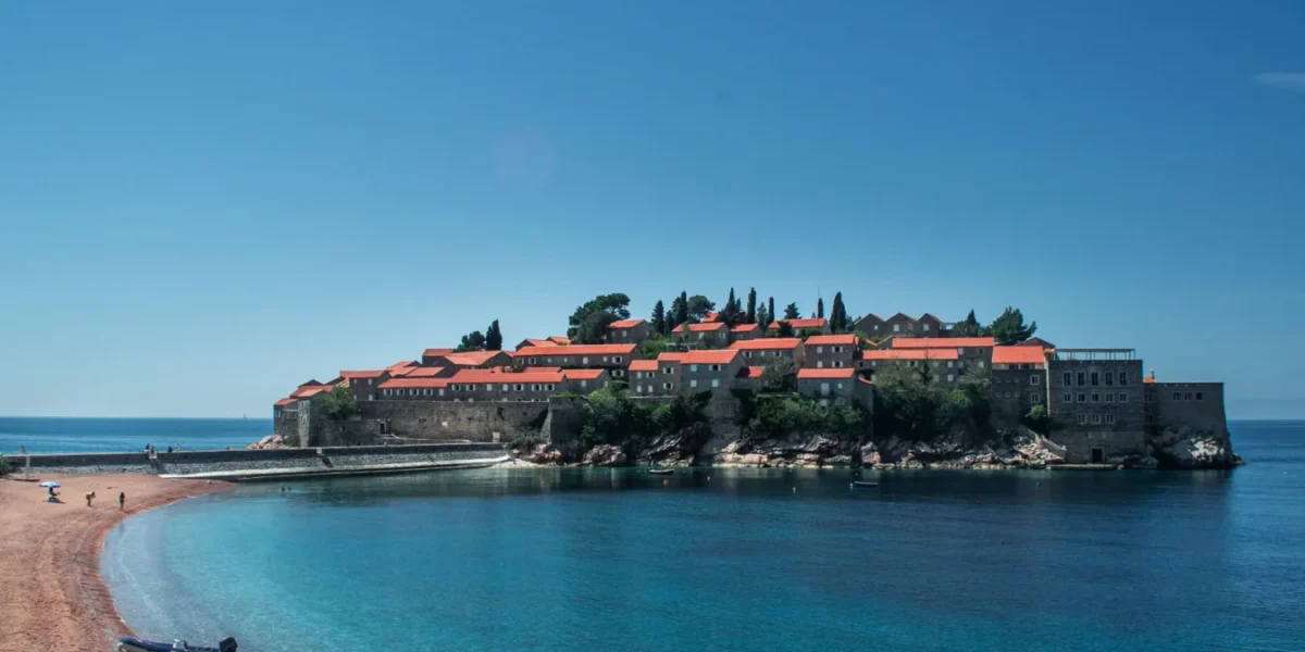 A breathtaking view of Sveti Stefan Island, Montenegro, surrounded by clear blue waters and a sandy beach.