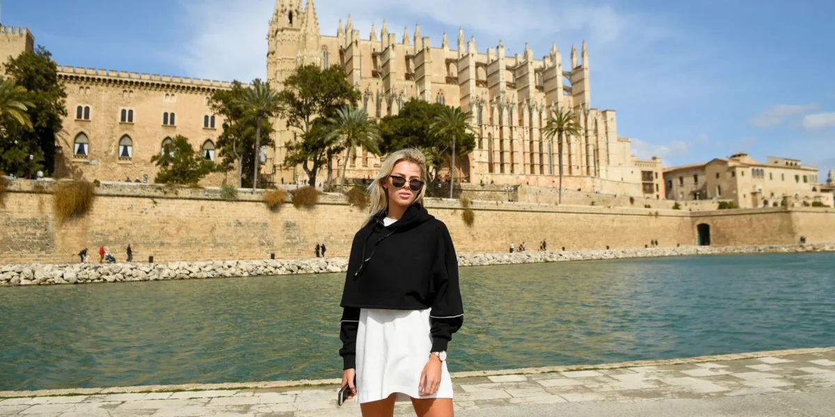 A woman poses with sunglasses in front of Palma Cathedral on a sunny day in Mallorca.