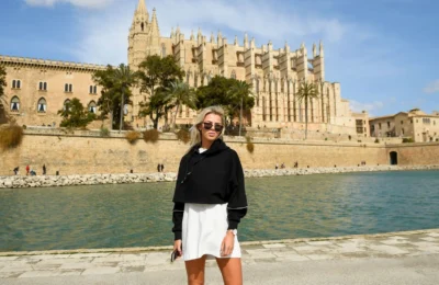 A woman poses with sunglasses in front of Palma Cathedral on a sunny day in Mallorca.