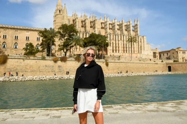 A woman poses with sunglasses in front of Palma Cathedral on a sunny day in Mallorca.