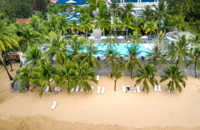 Aerial view of a tropical beachfront resort with palm trees, inviting pool, and sandy shore.