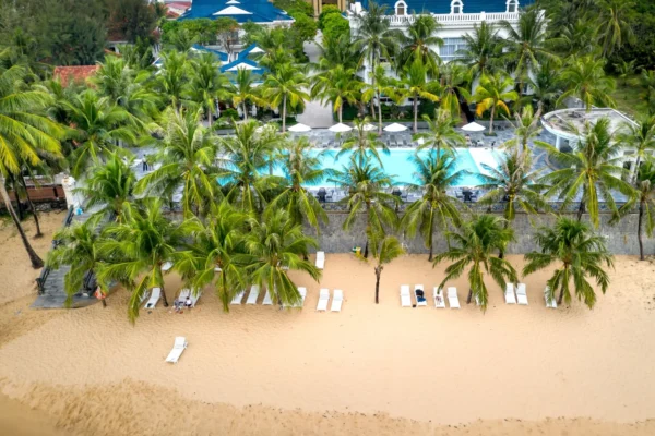 Aerial view of a tropical beachfront resort with palm trees, inviting pool, and sandy shore.