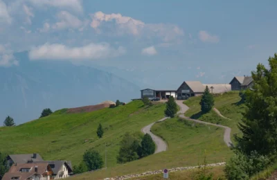 Beautiful alpine landscape with winding road and houses against a mountainous backdrop.