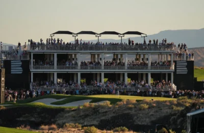 Large crowd gathers on multi-level viewing structure at a golf event during sunset.