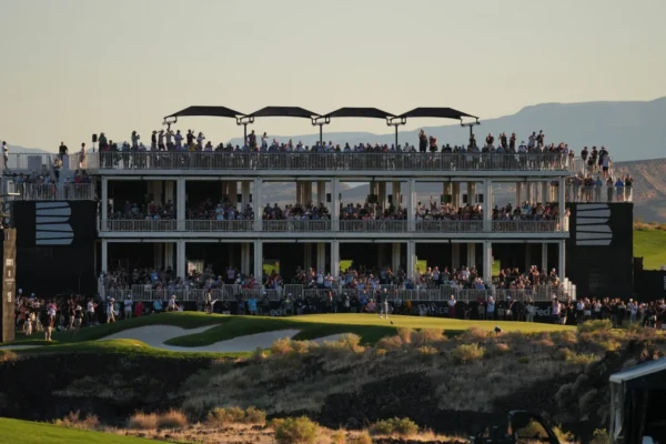 Large crowd gathers on multi-level viewing structure at a golf event during sunset.