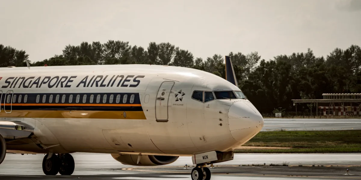 Singapore Airlines plane taxiing on airport runway under cloudy skies.