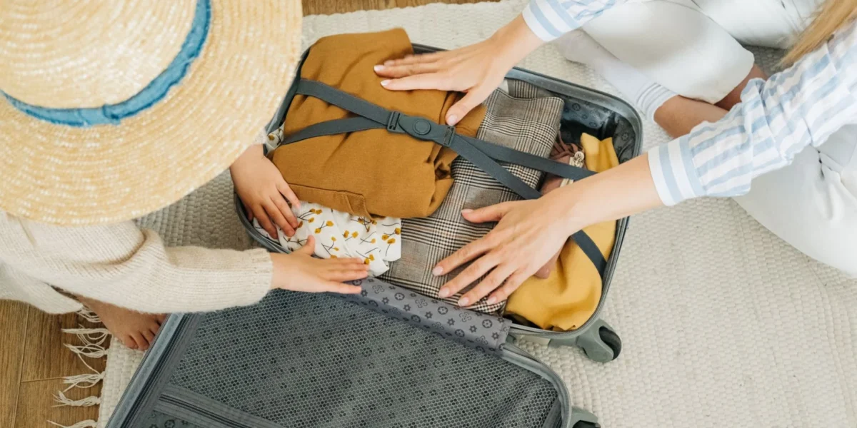A woman and child pack clothes in a suitcase, preparing for a vacation.