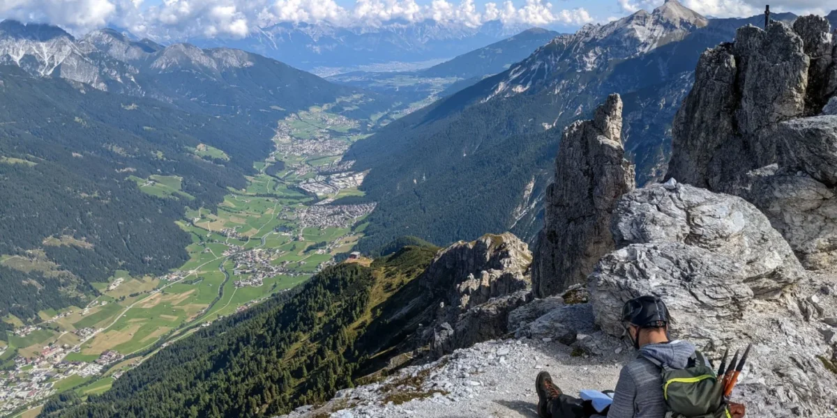 A hiker sitting on a rocky mountain edge in Tirol, Austria, enjoying a breathtaking valley view.