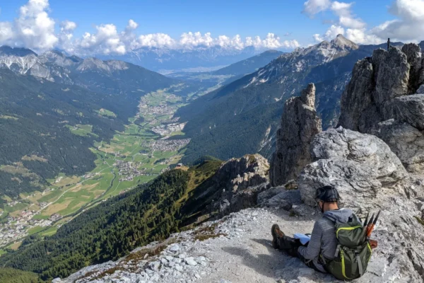 A hiker sitting on a rocky mountain edge in Tirol, Austria, enjoying a breathtaking valley view.