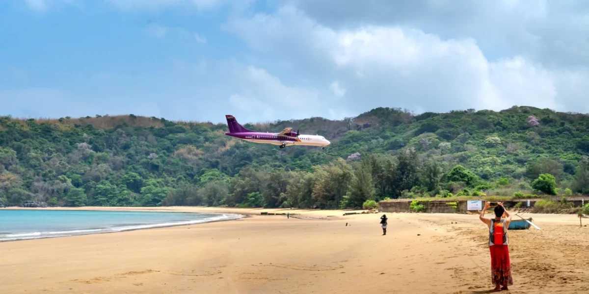 A plane approaches a beautiful tropical beach as people watch and take photos, capturing a unique travel moment.