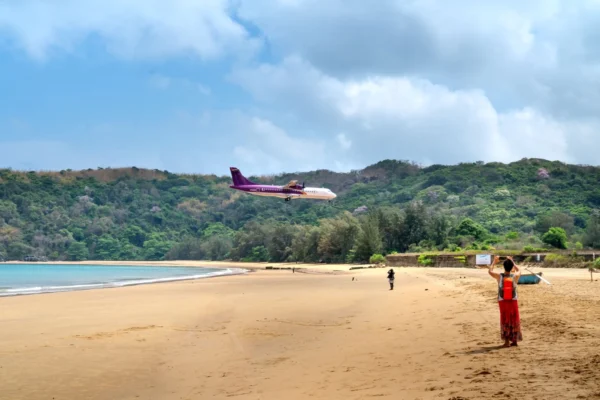 A plane approaches a beautiful tropical beach as people watch and take photos, capturing a unique travel moment.