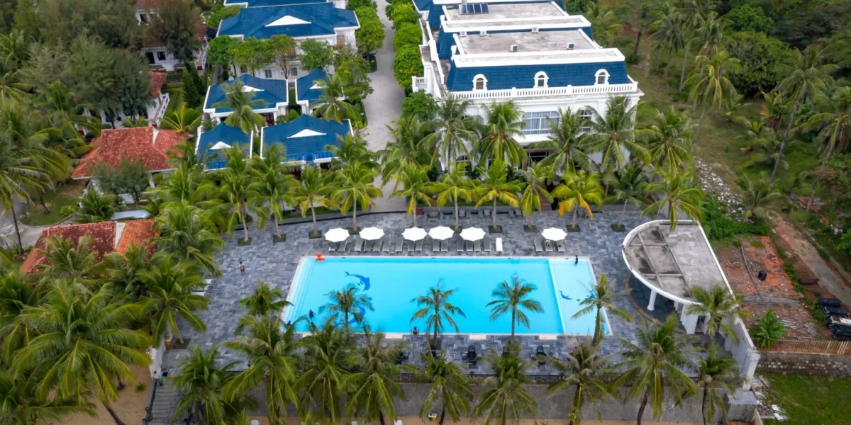 Stunning aerial view of a tropical resort, featuring a swimming pool and lush palm trees near the beach.
