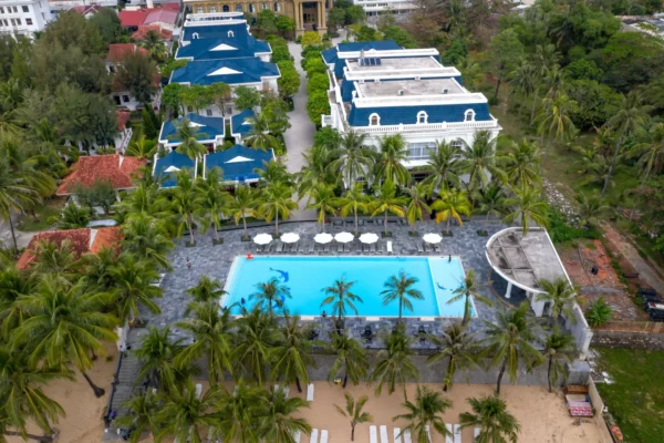 Stunning aerial view of a tropical resort, featuring a swimming pool and lush palm trees near the beach.