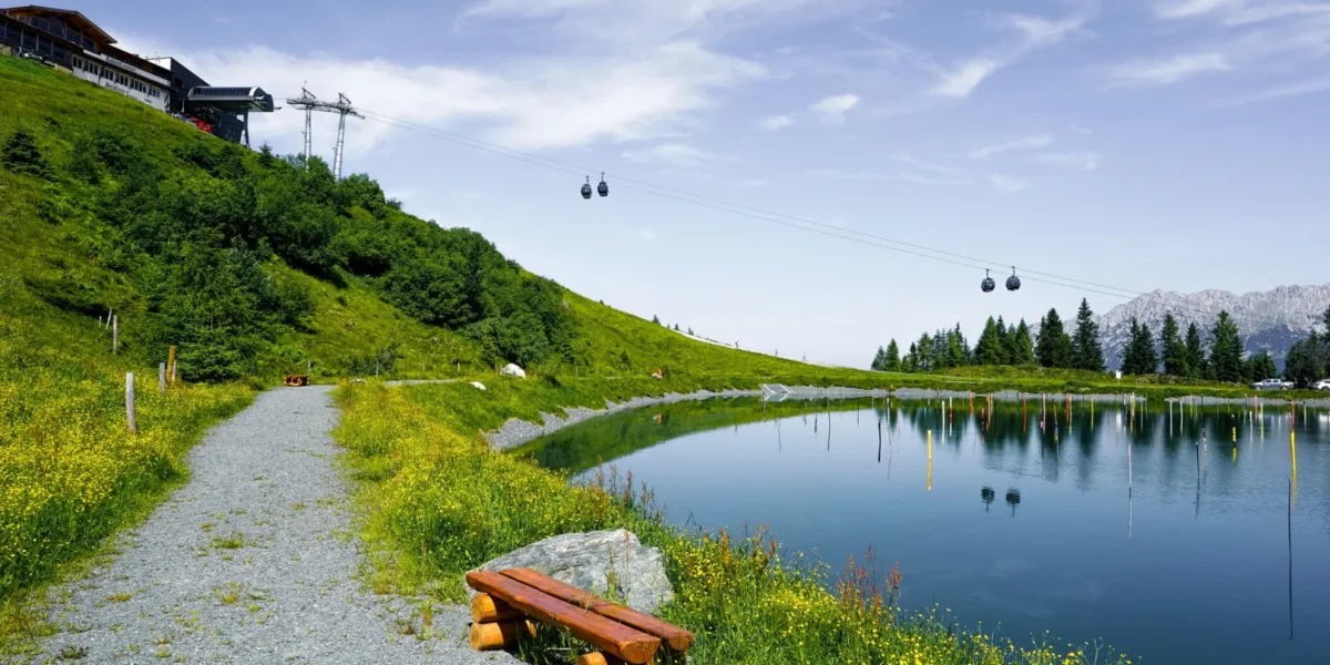 Idyllic summer scene with lake, cable cars, and vibrant green landscape in Ellmau, Austria.