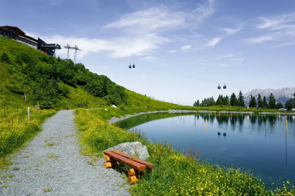 Idyllic summer scene with lake, cable cars, and vibrant green landscape in Ellmau, Austria.