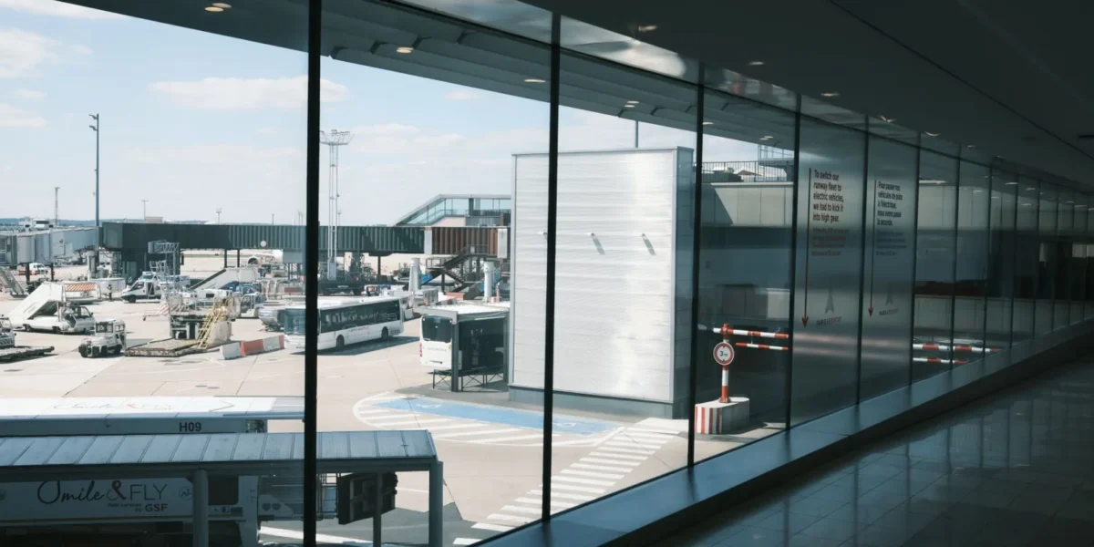 Wide view of an airport terminal hallway and tarmac, showcasing airplanes and buses.