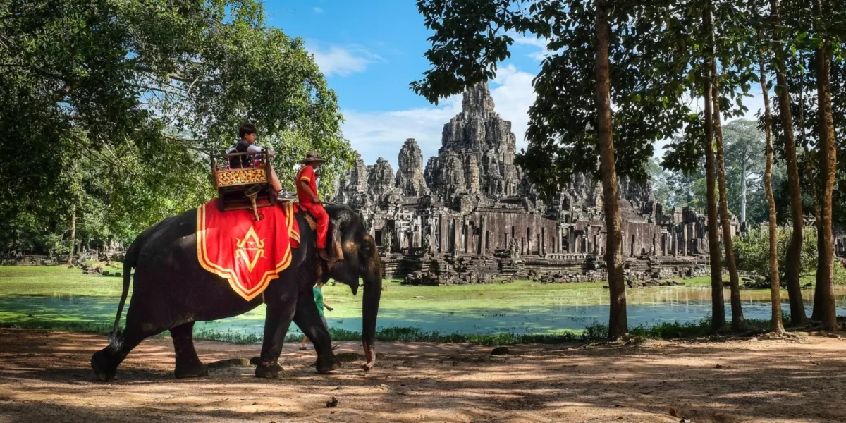 Elephant with riders at Bayon Temple in Cambodia showcasing cultural heritage and lush scenery.